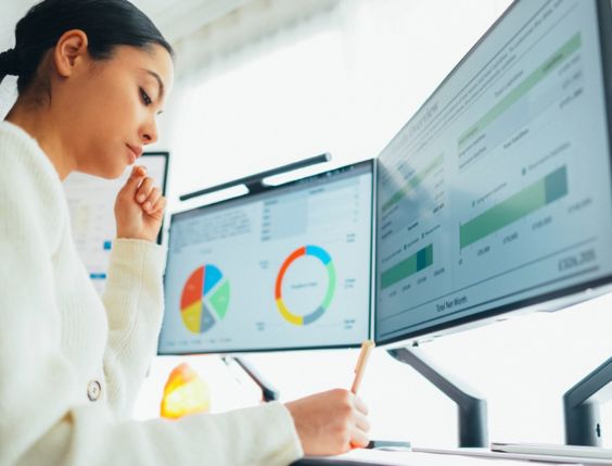 A woman working on a computer with a large screen displaying numbers and data, representing an employee in a Product Management role.